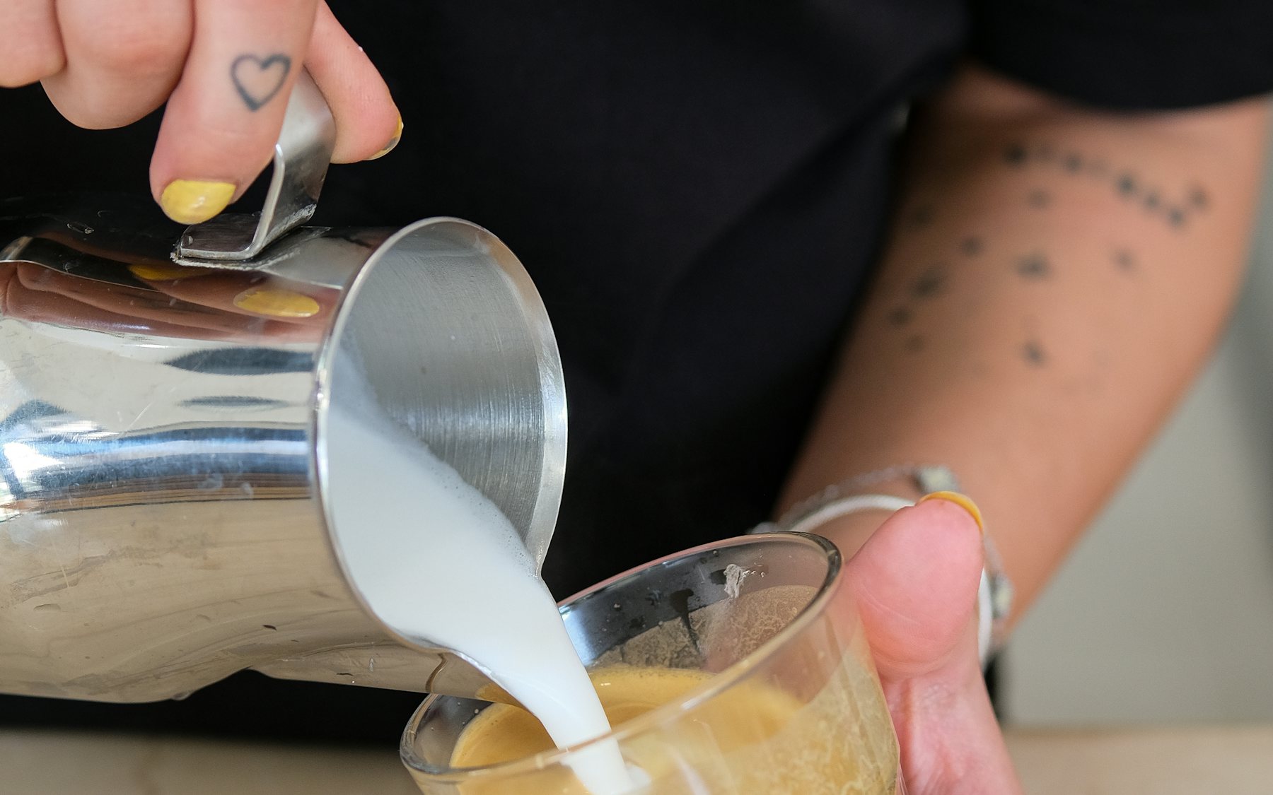 Kursgruppe an einem Tresen während einer Barista-Schulung, Trainerin zeigt auf die Maschine
